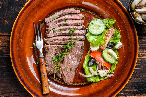 Grilled veal meat chop steak on a plate with salad. Dark wooden background. Top view. - 写真・画像