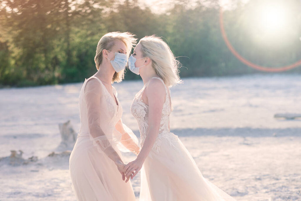 白い砂の上にレズビアンカップルの結婚式,流行を防ぐためにマスクを着用COVID-19 - 写真・画像