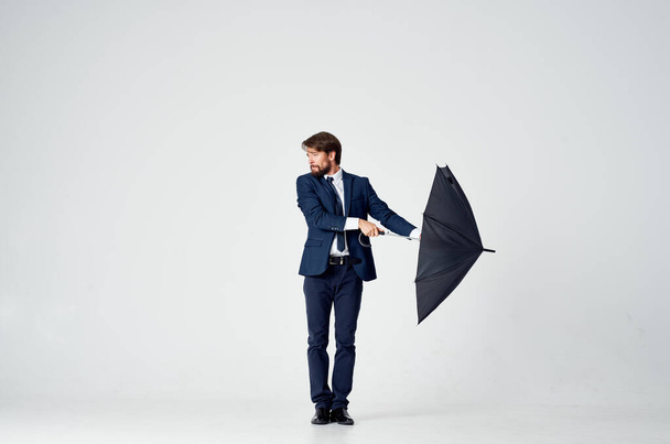 бизнесмен в костюме позирует на светлом фоне с черным зонтиком в руке - Фото, изображение