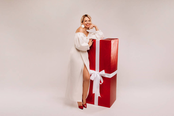 A girl in a white dress with a huge red gift on a white background smiles - Φωτογραφία, εικόνα