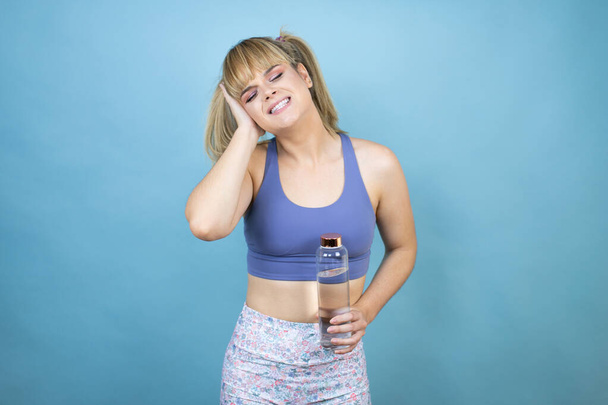 Young beautiful woman wearing sportswear holding a bottle of water over isolated blue background covering ears with hands with annoyed expression for the noise of loud music. Deaf concept. - Photo, Image