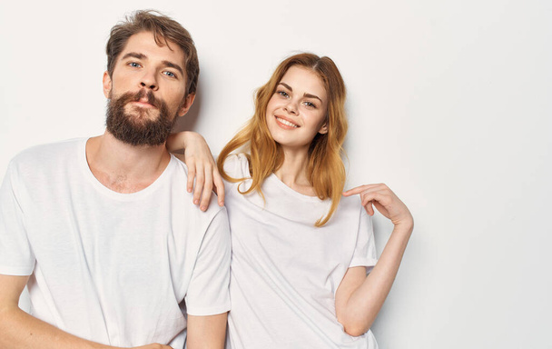 Ένα νεαρό ζευγάρι στέκεται δίπλα σε ένα λευκό μπλουζάκι από κοντά. - Φωτογραφία, εικόνα