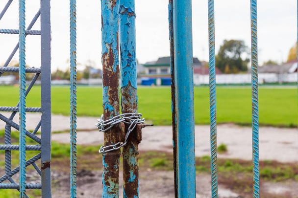The closed old shabby gates of the stadium, wrapped in a chain during the lockdown period in connection with the COVID-19 pandemic, the coronavirus infection. Background - Photo, Image