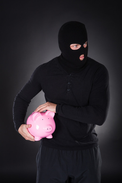Burglar stealing a pink piggy bank - Foto, Imagen