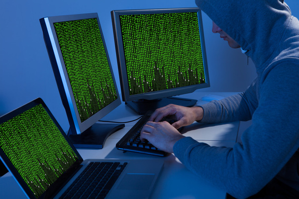 Hacker In Hooded Jacket Using Computer At Table - Fotografie, Obrázek