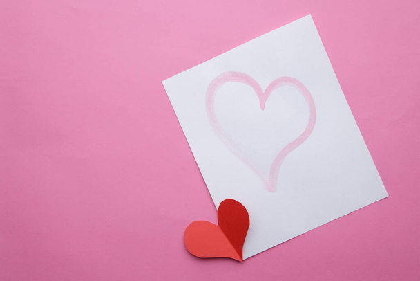 paper cut red heart lies next to leaf with pattern of hearts on pink background - Photo, image
