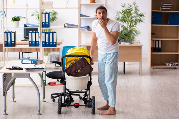 Joven empleado masculino que cuida del recién nacido en el lugar de trabajo - Foto, Imagen