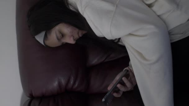 Młoda nastolatka odpoczywająca na kanapie przy użyciu smartfona podczas blokady. Pionowe wideo, zablokowane - Materiał filmowy, wideo
