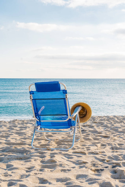 соломенная шляпа на синем стуле на пустынном пляже - Фото, изображение