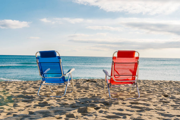 無人のビーチにある赤と青の椅子は - 写真・画像
