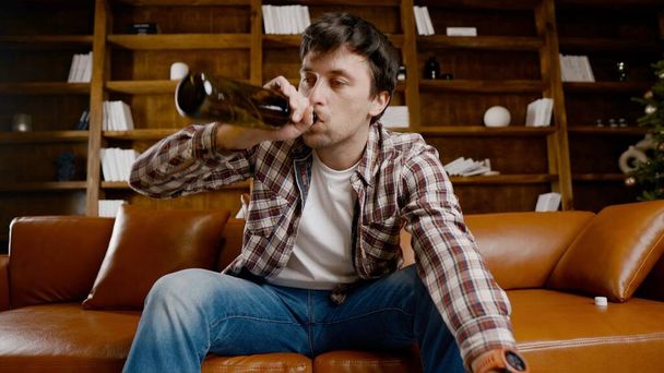 Alkoholsucht in jungen Jahren. Kaukasische Männer können nicht aufhören, Alkohol zu trinken, betrunkene einsame Männer trinken Wein aus der Flasche. Einsamkeit, Depression und Alkoholismus während der Weihnachts- und Neujahrsfeiertage. - Foto, Bild