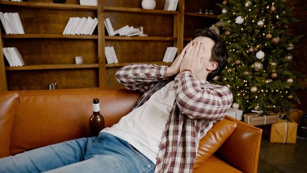 Alcohol addiction at young age. Caucasian male cannot stop drinking alcohol, drunken lonely male drinks wine from bottle. Loneliness, depression and alcoholism during Christmas and New Year holidays. - Photo, Image