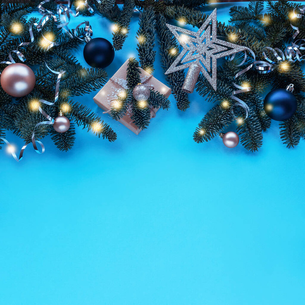 Fir branches, gift in a box and baubles on blue background with Christmas lights. Top view, flat lay, copy space. - Photo, Image