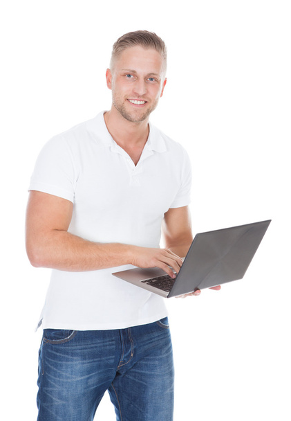 Улыбающийся человек в джинсах, стоящий с помощью портативного компьютера
 - Фото, изображение