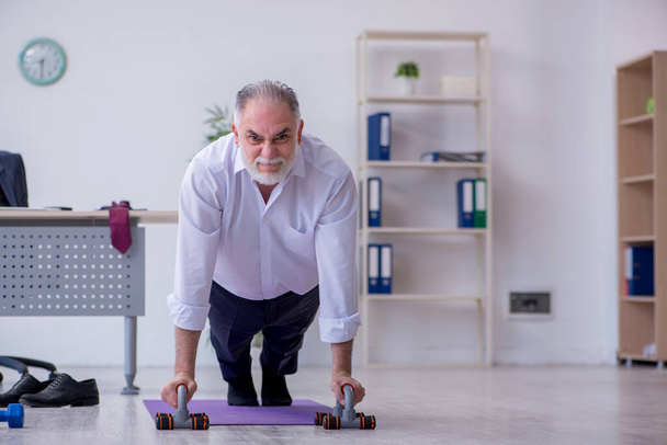 Empleado varón envejecido haciendo ejercicios físicos durante el descanso - Foto, imagen