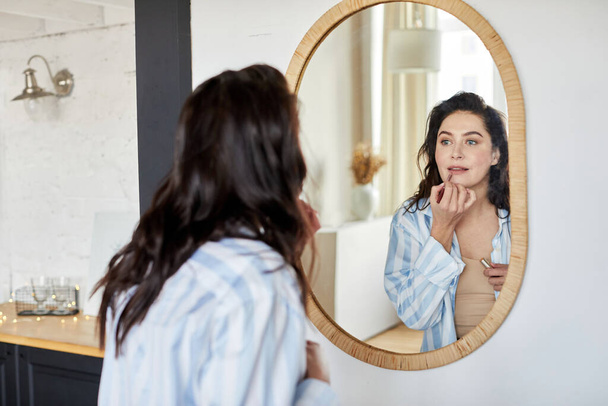 Kobieta nakładająca makijaż w pobliżu lustra - Zdjęcie, obraz