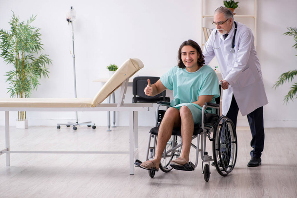 Paciente masculino joven en silla de ruedas y traumatólogo médico experimentado - Foto, Imagen