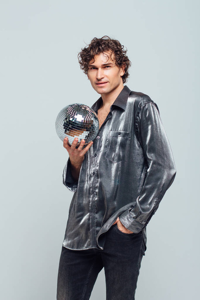 Portrait of tall attractive man with a mirror disco ball on a white background. Handsome man posing with a shiny disco ball in studio. - Фото, зображення