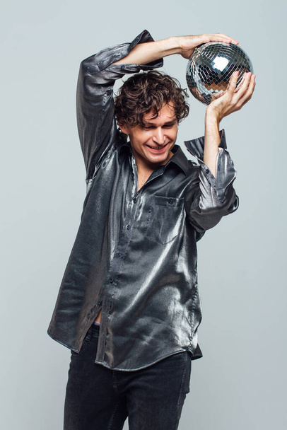 Portrait of tall attractive man with a mirror disco ball on a white background. Handsome man posing with a shiny disco ball in studio. - Фото, зображення
