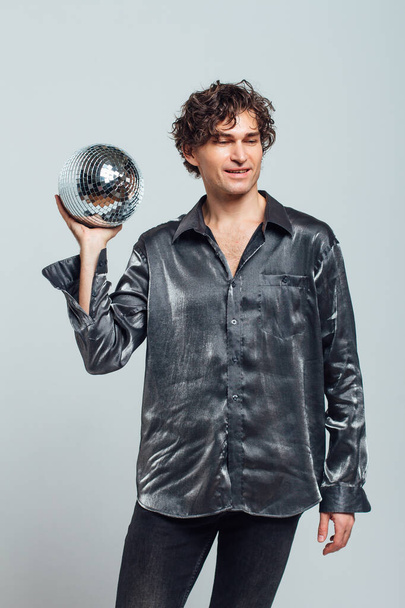 Portrait of tall attractive man with a mirror disco ball on a white background. Handsome man posing with a shiny disco ball in studio. - Photo, image