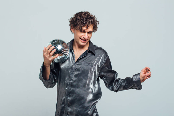 Portrait of tall attractive man with a mirror disco ball on a white background. Handsome man posing with a shiny disco ball in studio. - Фото, изображение