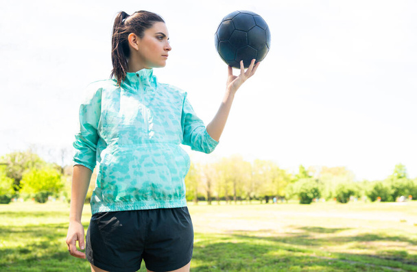 Young female soccer player standing on field holding ball. - Φωτογραφία, εικόνα