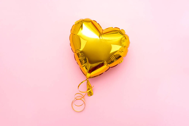 Golden heart foil balloon upper view on pink Valentines Day background. Copyspace - Фото, изображение