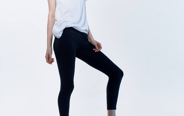 Woman indoors on a light background and black leggings in a white t-shirt - Photo, Image