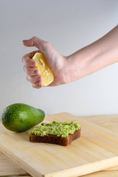 Жінка стискає половину лимона на цілому тості авокадо хліба
. - Фото, зображення