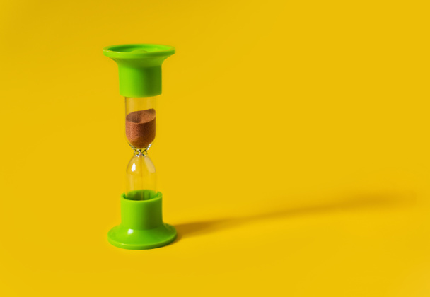 明るい黄色の背景に電球を介して実行砂と緑の医療用砂時計。時間は速く、カウントダウン、締め切り、通過時間、概念を測定します。テキストのコピースペース. - 写真・画像