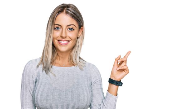 Beautiful blonde woman wearing casual clothes with a big smile on face, pointing with hand finger to the side looking at the camera.  - Photo, Image