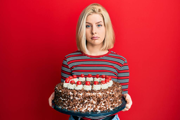 Jonge blonde vrouw vieren verjaardag met grote chocoladetaart depressief en zorgen voor verdriet, huilen boos en bang. trieste uitdrukking.  - Foto, afbeelding
