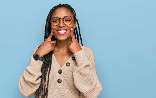 Αφροαμερικανή που φοράει καθημερινά ρούχα χαμογελώντας με ανοιχτό στόμα, δείχνοντας με τα δάχτυλα και αναγκάζοντας το χαρούμενο χαμόγελο  - Φωτογραφία, εικόνα