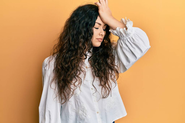 Young brunette woman with curly hair wearing casual clothes surprised with hand on head for mistake, remember error. forgot, bad memory concept.  - Photo, Image