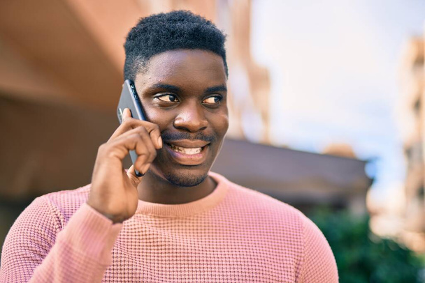 Jovem afro-americano sorrindo feliz falando no smartphone da cidade. - Foto, Imagem