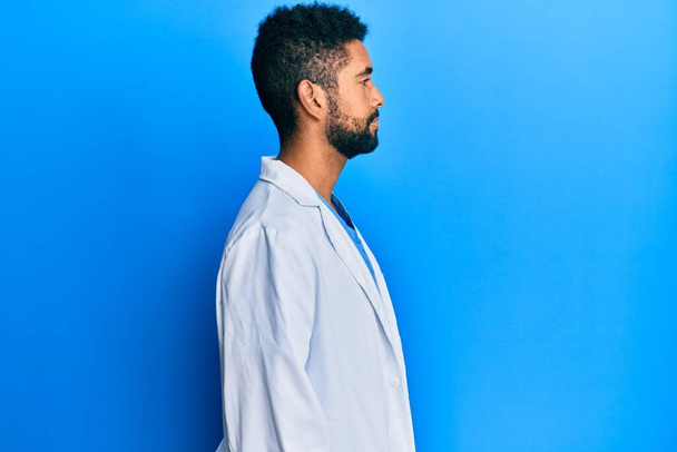 Handsome hispanic man with beard wearing doctor uniform looking to side, relax profile pose with natural face with confident smile.  - Foto, immagini