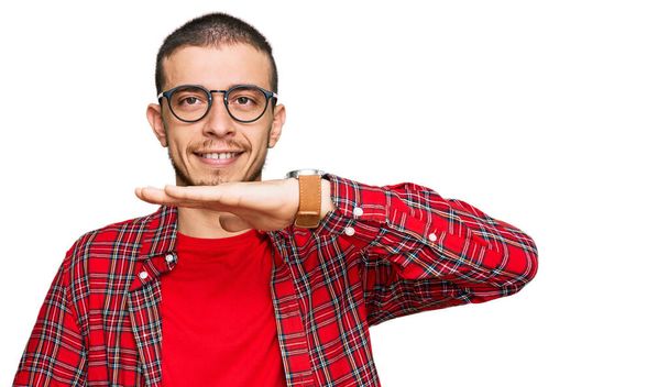 Hispánský mladý muž v neformálním oblečení gestikuluje s rukama ukazujícími velkou a velkou značku velikosti, symbol míry. s úsměvem na kameru. koncepce měření.  - Fotografie, Obrázek