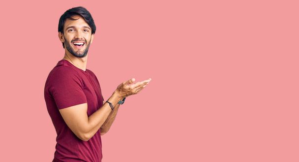 Красивый латиноамериканец в повседневной одежде, указывая в сторону с открытыми руками ладонями, показывая пространство для копирования, представляя рекламу улыбаясь взволнованной счастливой  - Фото, изображение