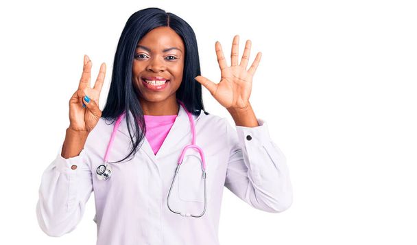 Doktor steteskobu takan Afro-Amerikalı genç bir kadın sekiz numaralı parmaklarını gösterip işaret ederken kendinden emin ve mutlu gülümsüyor..  - Fotoğraf, Görsel