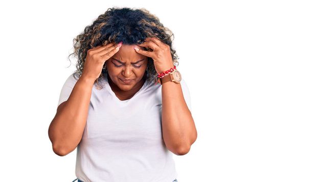 Giovane afroamericana plus size donna indossa abiti casual con mano sulla testa per il dolore alla testa perché lo stress. emicrania.  - Foto, immagini