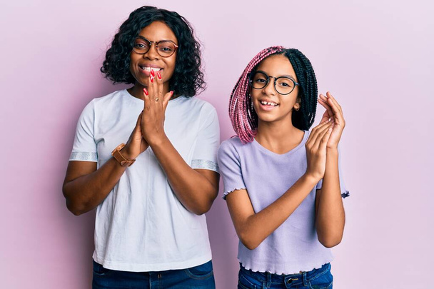 Прекрасна афро-американська мати і дочка, одягнені в повсякденний одяг і окуляри плескаючи і аплодуючи щасливі і радісні, посміхаючись горді руки разом.  - Фото, зображення