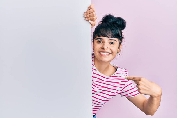 Junges hispanisches Mädchen mit leerem Transparent, das mit dem Finger auf ein sich selbst lächelndes glückliches und stolzes Mädchen zeigt  - Foto, Bild