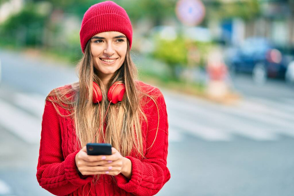Junge hispanische Frau mit Smartphone und Kopfhörer in der Stadt. - Foto, Bild