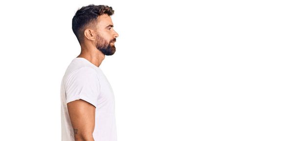 Fiatal spanyol férfi visel alkalmi fehér póló néz oldalra, pihenni profil pózol természetes arc magabiztos mosollyal.  - Fotó, kép