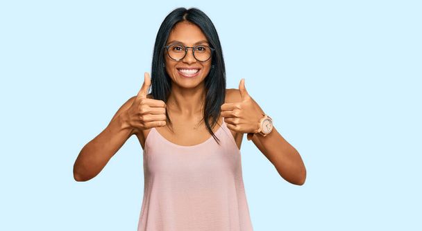 若いアフリカ系アメリカ人の女性は、カジュアルな服や眼鏡の成功のサインを手で積極的なジェスチャーを行う着て、親指を笑顔と幸せ。陽気な表情と勝者のジェスチャー.  - 写真・画像