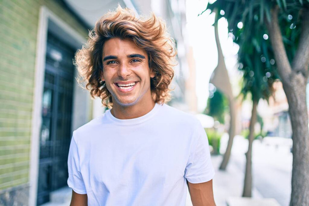 Jonge knappe Latijns-Amerikaanse man glimlachend gelukkig wandelen op straat van de stad - Foto, afbeelding