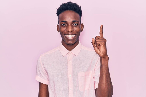 Mladý africký Američan v neformálním oblečení ukazuje prstem nahoru s úspěšným nápadem. odešel a byl šťastný. číslo jedna.  - Fotografie, Obrázek