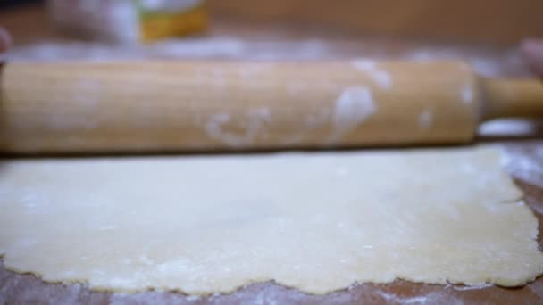 Les mains féminines déroulent la pâte sur la table en bois avec la broche à rouler dans la cuisine à la maison - Séquence, vidéo