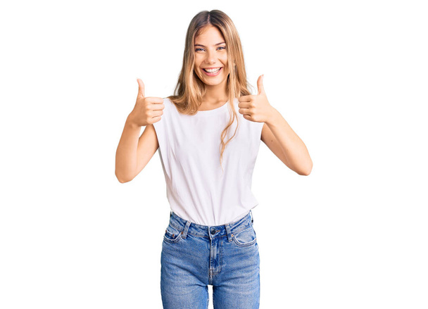 Beautiful caucasian woman with blonde hair wearing casual white tshirt success sign doing positive gesture with hand, thumbs up smiling and happy. cheerful expression and winner gesture.  - Фото, зображення