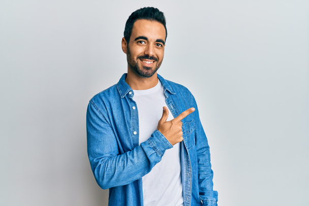 Fiatal spanyol férfi alkalmi ruhát visel mosolygós vidám mutató kéz és ujj fel az oldalra  - Fotó, kép